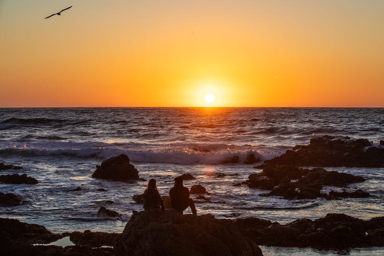 couple enjoying sunset on rocky ocean shore